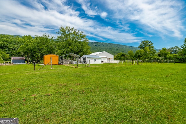 view of yard featuring a storage unit, a detached carport, a mountain view, fence, and an outdoor structure