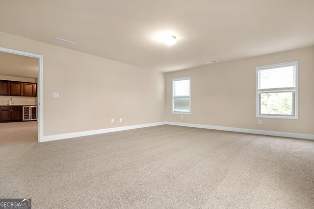 carpeted empty room with beverage cooler, sink, and plenty of natural light