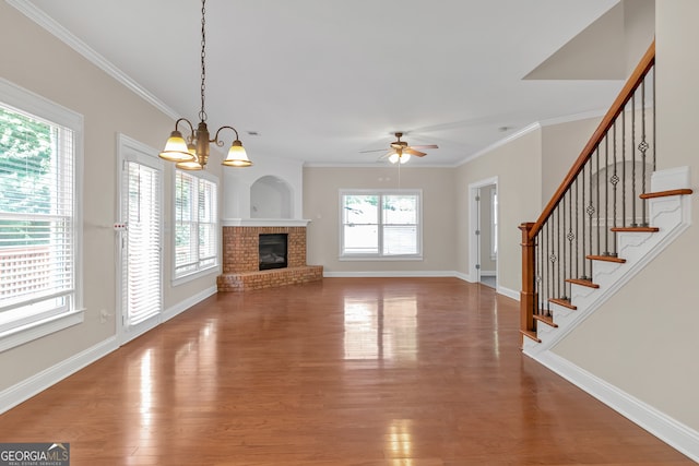 unfurnished living room with ceiling fan with notable chandelier, a fireplace, crown molding, and wood-type flooring