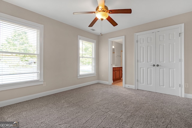 unfurnished bedroom with ceiling fan, ensuite bath, light carpet, and a closet