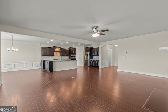 unfurnished living room with ceiling fan with notable chandelier and dark wood-type flooring