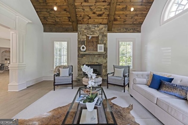 living room featuring light wood-type flooring, a stone fireplace, wood ceiling, high vaulted ceiling, and ornate columns