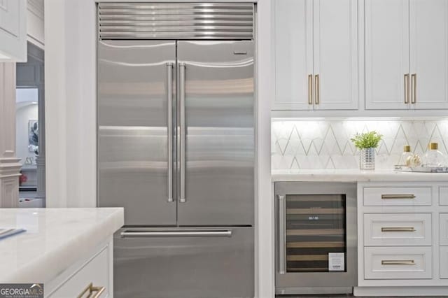 kitchen featuring tasteful backsplash, beverage cooler, white cabinets, built in fridge, and light stone countertops