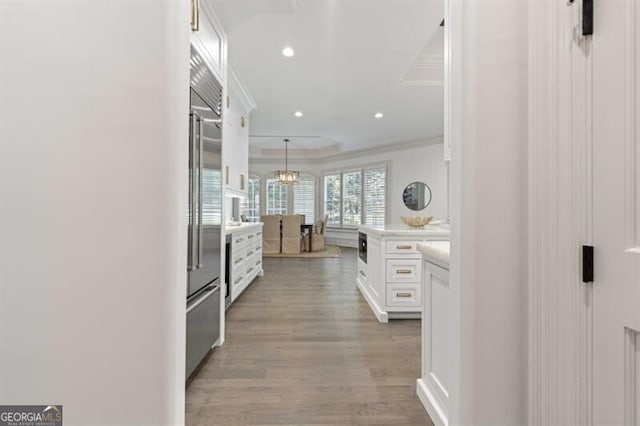 kitchen featuring light hardwood / wood-style flooring, white cabinetry, crown molding, stainless steel built in fridge, and hanging light fixtures