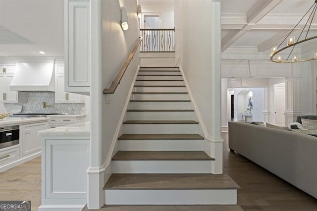 stairway with beamed ceiling, hardwood / wood-style flooring, coffered ceiling, and a notable chandelier