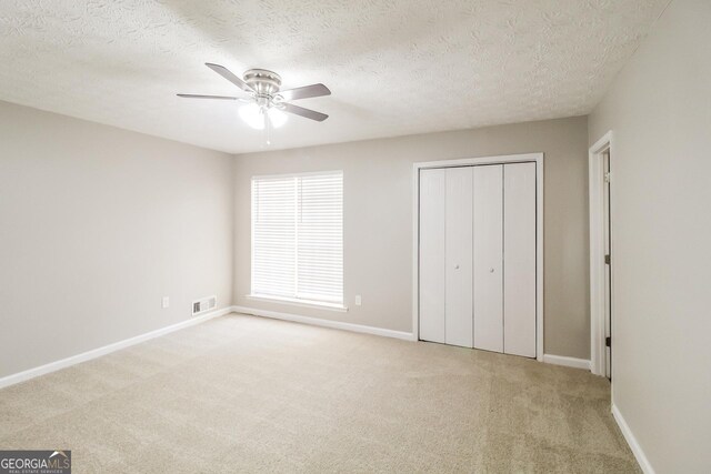 unfurnished bedroom with a textured ceiling, light colored carpet, and ceiling fan