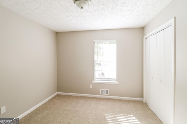 unfurnished bedroom featuring light carpet, a textured ceiling, and a closet