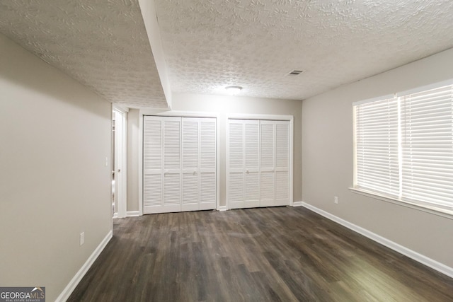 unfurnished bedroom featuring multiple closets, dark wood-type flooring, and a textured ceiling