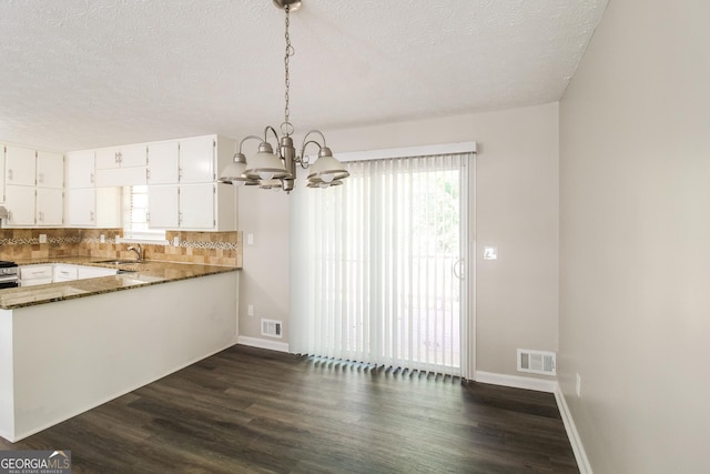 kitchen featuring sink, dark stone countertops, a textured ceiling, white cabinets, and decorative light fixtures