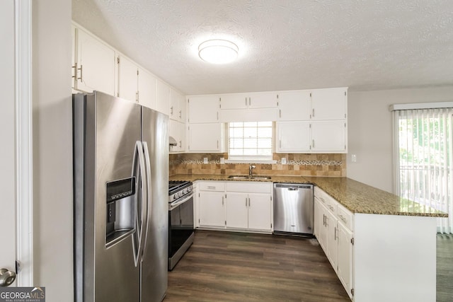 kitchen featuring appliances with stainless steel finishes, white cabinets, dark stone counters, and kitchen peninsula