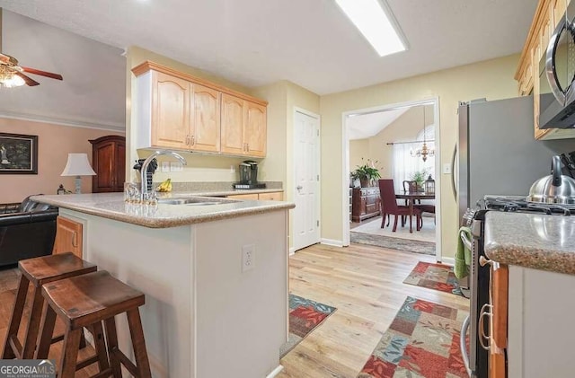 kitchen with appliances with stainless steel finishes, a kitchen breakfast bar, light hardwood / wood-style floors, kitchen peninsula, and light brown cabinets