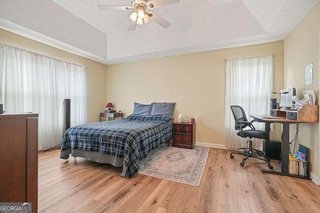 bedroom with light hardwood / wood-style flooring, ceiling fan, and a raised ceiling