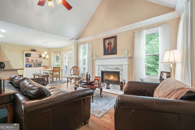 living room with high vaulted ceiling, a textured ceiling, ceiling fan, light hardwood / wood-style flooring, and a premium fireplace