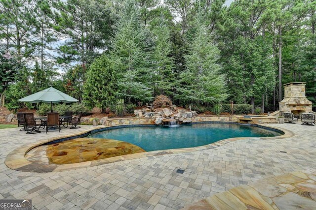 view of swimming pool featuring a patio, an outdoor stone fireplace, and pool water feature