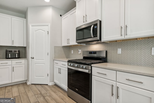 kitchen with backsplash, light stone counters, light hardwood / wood-style floors, stainless steel appliances, and white cabinets