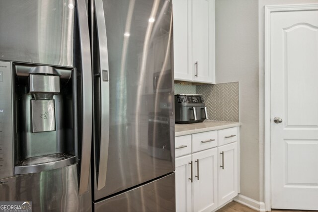 kitchen featuring backsplash, stainless steel fridge with ice dispenser, light wood-type flooring, and white cabinetry