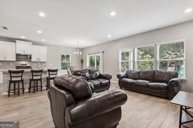 living room with light wood-type flooring, sink, a notable chandelier, and plenty of natural light