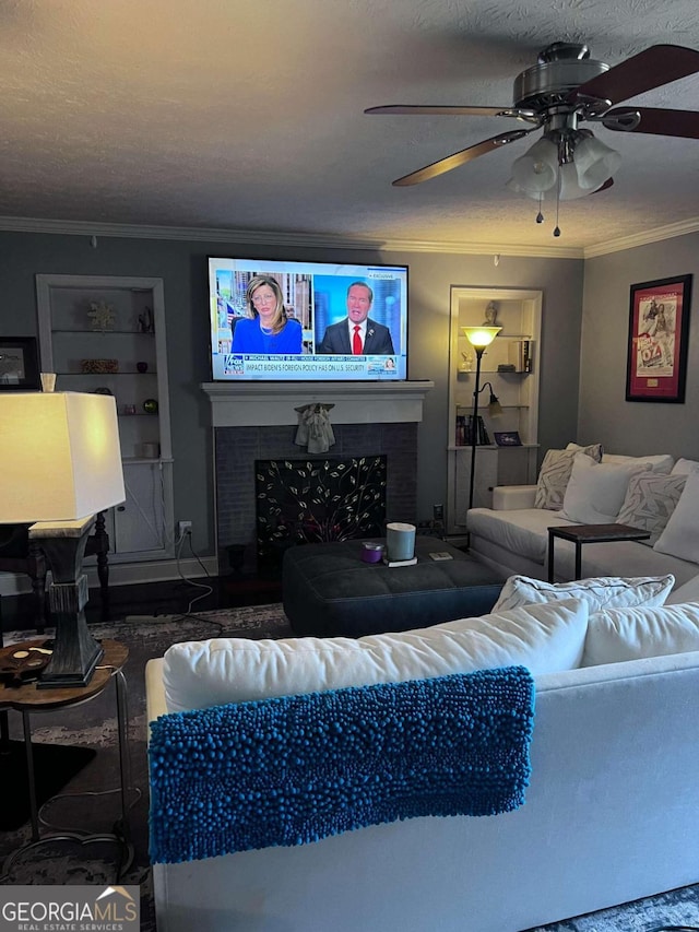 living room featuring ceiling fan, ornamental molding, a textured ceiling, and a brick fireplace