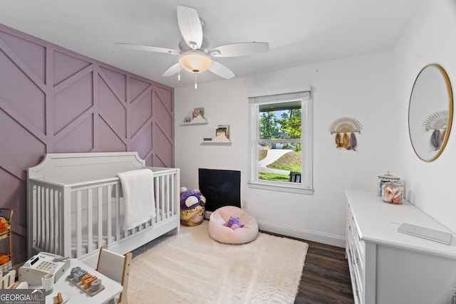 bedroom with dark hardwood / wood-style flooring, a crib, and ceiling fan