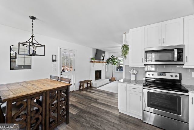 kitchen with backsplash, dark hardwood / wood-style flooring, a fireplace, appliances with stainless steel finishes, and light stone counters