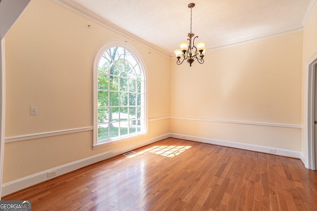 spare room with wood-type flooring, ornamental molding, and a notable chandelier