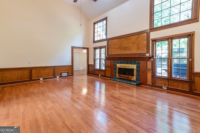 unfurnished living room featuring light wood-type flooring, high vaulted ceiling, ceiling fan, and a tile fireplace