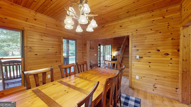 dining space featuring light hardwood / wood-style flooring, wooden walls, a notable chandelier, and wooden ceiling