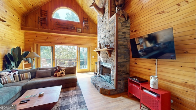 living room with wooden walls, high vaulted ceiling, a stone fireplace, and wood-type flooring