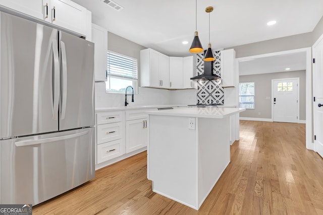 kitchen with wall chimney range hood, white cabinets, a kitchen island, and stainless steel refrigerator