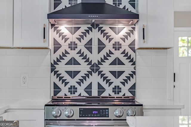 kitchen with wall chimney exhaust hood, white cabinetry, decorative backsplash, and stainless steel range oven