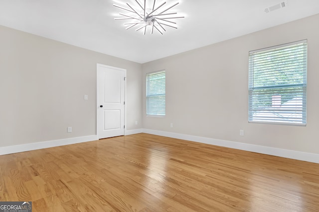 spare room featuring light wood-type flooring and a notable chandelier