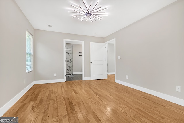 unfurnished bedroom featuring a walk in closet, light wood-type flooring, and a chandelier