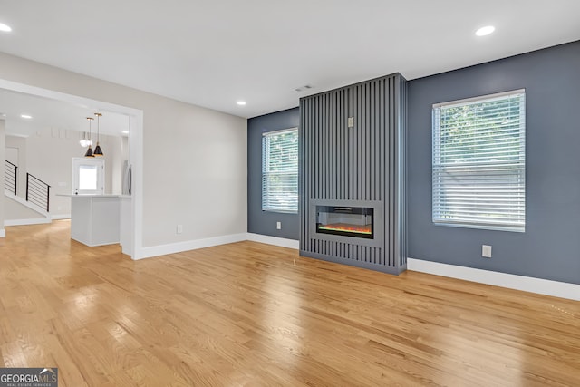 unfurnished living room featuring a healthy amount of sunlight, a large fireplace, and light hardwood / wood-style flooring