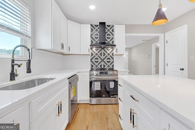 kitchen featuring light hardwood / wood-style flooring, decorative light fixtures, stainless steel appliances, sink, and wall chimney range hood