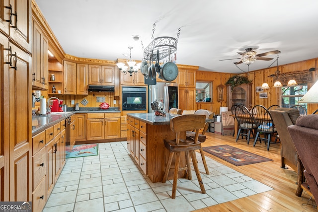 kitchen with black appliances, light wood-type flooring, ceiling fan with notable chandelier, a kitchen breakfast bar, and a center island