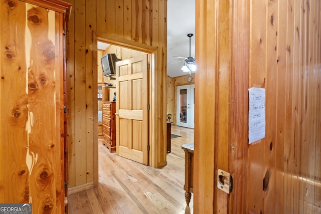 corridor with light hardwood / wood-style flooring and wooden walls