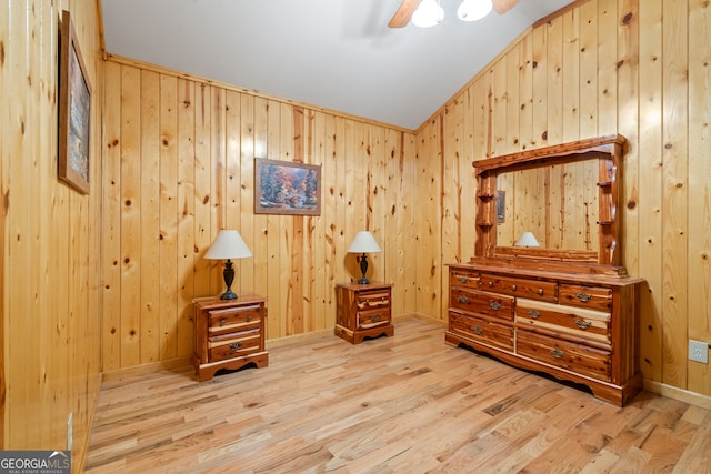 interior space with vaulted ceiling, light wood-type flooring, wood walls, and ceiling fan