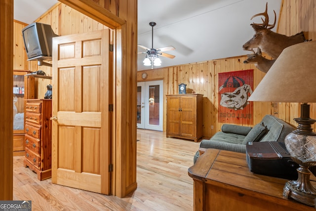 living room with ceiling fan, light hardwood / wood-style flooring, wooden walls, and french doors