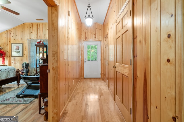 hall with light hardwood / wood-style flooring, vaulted ceiling, and wooden walls