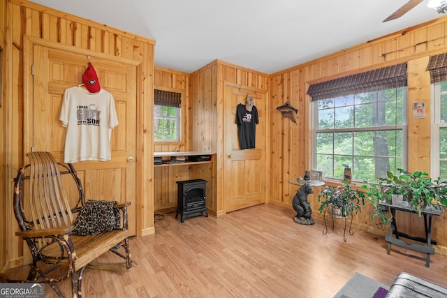 sitting room with ceiling fan, wooden walls, a wood stove, and light wood-type flooring