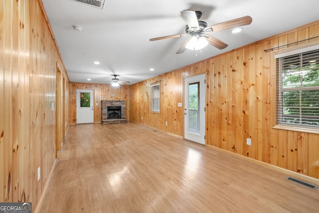 unfurnished living room featuring a fireplace, light wood-type flooring, wood walls, and a wealth of natural light