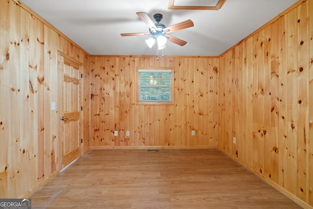 spare room with ceiling fan, wooden walls, and light hardwood / wood-style floors