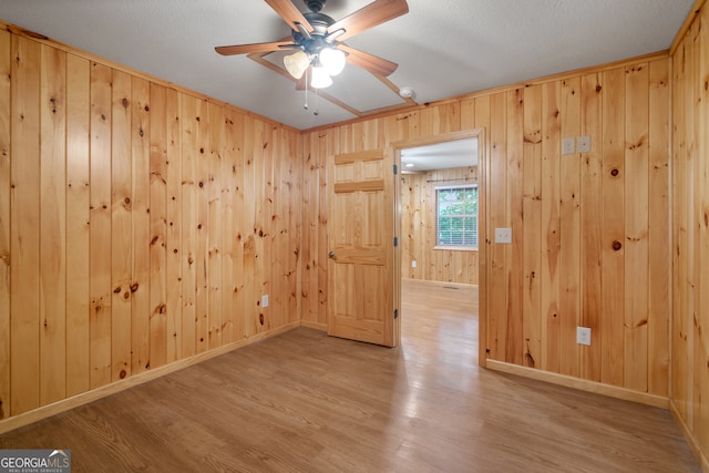 spare room featuring light wood-type flooring, ceiling fan, a textured ceiling, and wood walls