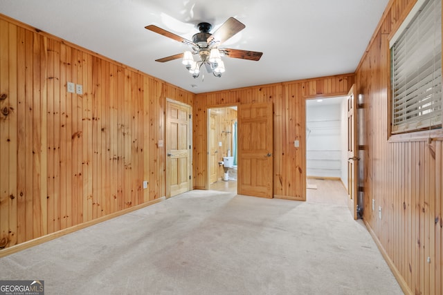 unfurnished bedroom featuring wood walls, a walk in closet, ceiling fan, and light carpet