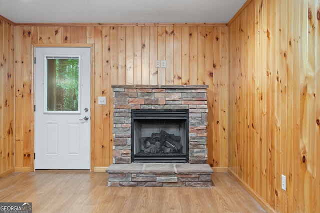 unfurnished living room with wood walls, light hardwood / wood-style floors, and a stone fireplace