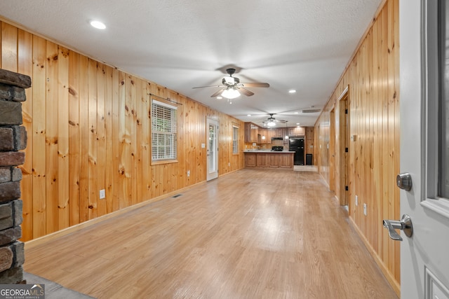 interior space with ceiling fan, light wood-type flooring, wood walls, and a textured ceiling