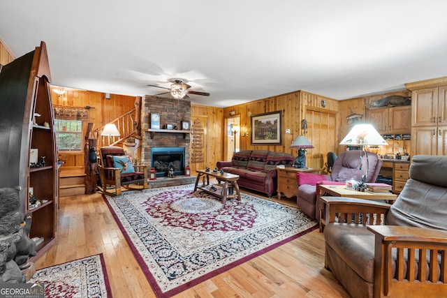 living room featuring ceiling fan, wood walls, light hardwood / wood-style flooring, and a stone fireplace