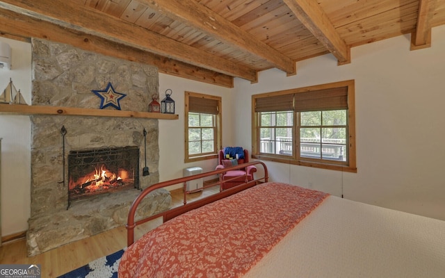 bedroom featuring beam ceiling, wooden ceiling, a stone fireplace, and hardwood / wood-style flooring