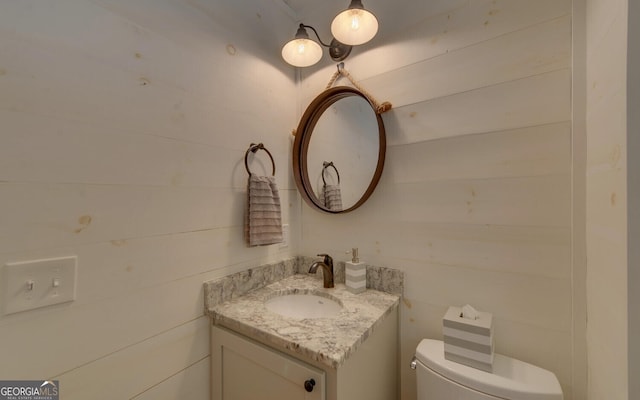 bathroom featuring wooden walls, toilet, and vanity