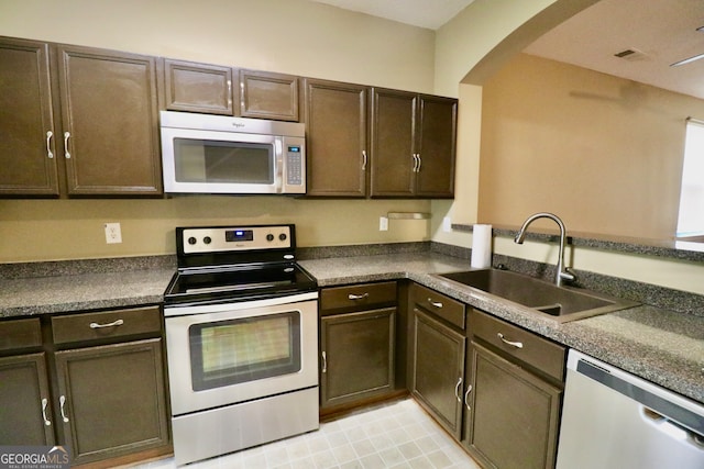 kitchen with stainless steel appliances, dark brown cabinets, sink, light tile patterned floors, and kitchen peninsula